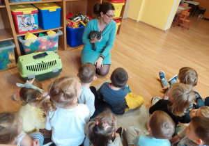 Dzieci siedzą na dywanie i słuchają opowiadania nauczycielki.
