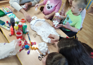 Dzieci smarują tekturowy kontur dyni za pomocą kleju oraz przyklejają watę.