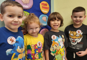Trzech chłopców i dziewczynka uśmiechają się do zdjęcia, do koszulek mają przypięte plakietki z okazji Dnia Misia