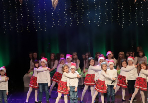Dzieci z grupy Biedroneczki na scenie KDK podczas wykonywania piosenki "Mikołaj i katar"- dziewczynki przytulają chłopców.