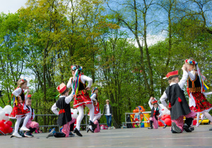 Dzieci z grupy Biedroneczki podczas obchodów Święta Konstytucji 3 maja tańczą krakowiaka na scenie w Parku Traugutta.