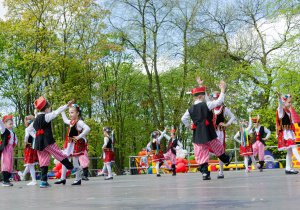 Dzieci z grupy Biedroneczki podczas obchodów Święta Konstytucji 3 maja tańczą krakowiaka na scenie w Parku Traugutta.