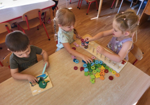 Dzieci siedzą przy stoliku i układają drewniane układanki.