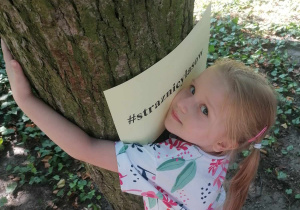 Dziewczynka przytula się do drzewa.
