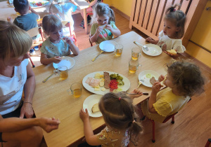 Dzieci siedzą przy stole i częstują się produktami spożywczymi. leżącymi na wspólnej tacy
