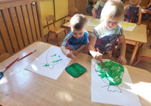 Dwoje dzieci maluje pędzelkiem worek.