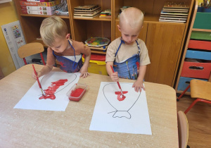 Dwoje chłopców maluje pędzelkiem worek.