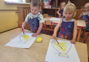 Dwoje dzieci maluje pędzlekiem worek.