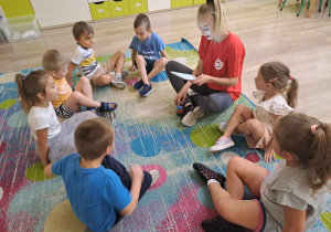 Dzieci siedzą na dywanie z instruktorem.