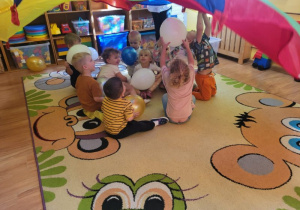 Dzieci uczestniczą w zabawie z chustą animacyjną i balonami.