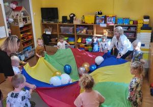 Dzieci uczestniczą w zabawie z chustą animacyjną i balonami.