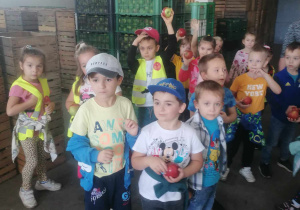 Dzieci stoją przy skrzyniach z jabłkami.