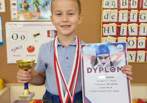 Chłopiec prezentuje zdobyte medale, puchar oraz dyplom