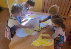 Dzieci malują żółtą farbą sylwetę gruszki.