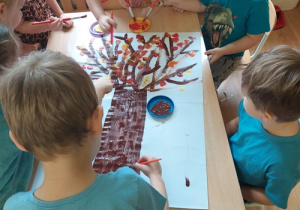 Dzieci malują farbami jesienne drzewo.