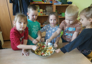 Dzieci wykonują sałatkę owocową.