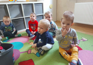 Dzieci siedzą na dywanie podczas zajęć.