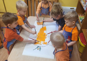 Dzieci malują farbą plakatową sylwety marchewki w zespołach.
