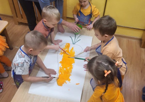 Dzieci malują farbą plakatową sylwety marchewki w zespołach.