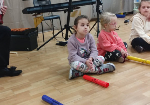Dzieci siedzą na podłodze przy instrumentach muzycznych.