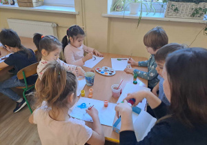 Dzieci malują farbami przy stolikach.