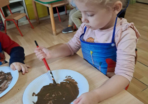 Dziewczynka maluje farbą papierowy talerzyk.