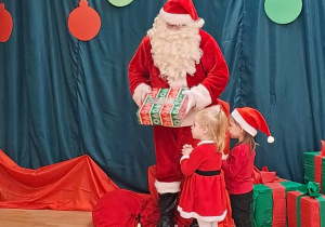 Dziewczynki dziękują Mikołajowi i wręczają mu upominek.