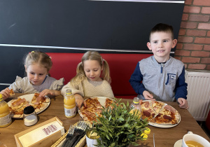 Dzieci jedzą własnoręcznie przygotowaną pizzę.