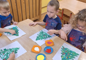 Palcami umoczonymi z farbach różnego koloru dzieci ozdabiały swoje choinki.