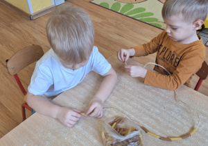 Franek i Stefan nawlekają na sznurek rurki makaronowe tworząc łańcuch na sensoryczną choinkę.