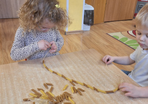 Dzieci nawlekają na sznurek rurki makaronowe tworząc łańcuch na sensoryczną choinkę.