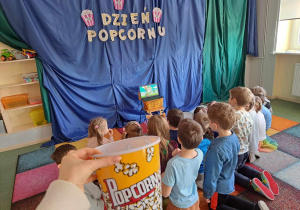 Dzieci zajadają popcorn i oglądają bajkę.