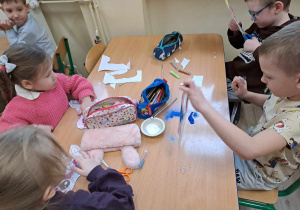 Dzieci przy stolikach wykonują maski karnawałowe.