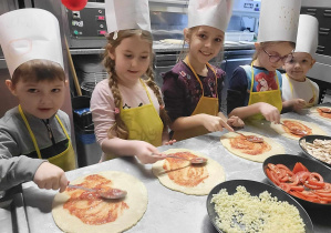 Dzieci biorą udział w warsztatach z robienia pizzy.