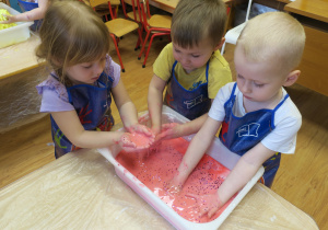 Dzieci bawią się masą, którą wymieszały z czerwonym barwnikiem.