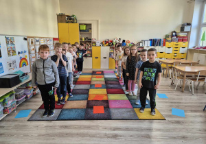 Dzieci stoją na dywanie w dwóch rzędach