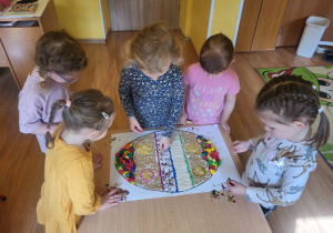 Dziewczynki ozdabiają pisankę używając kolorowych cekinów.