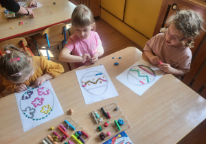 Marianna, Hania i Nina wykonują wzorki na konturze pisanki używając plasteliny.