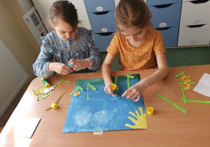 Dwie dziewczynki przyklejają elementy na karton.