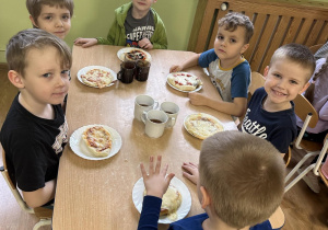 Dzieci siedzą przy stole z własnymi upieczonymi pizzami