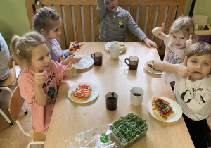 Dzieci siedzą przy stole i układają na pizzach ulubione składniki