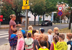 Dzieci oglądają znaki drogowe umieszczone przed przejściem dla pieszych w pobliżu szkoły.