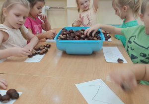 Dzieci wykonują zadanie z użyciem kasztanów.