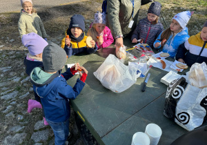 Dzieci jedzą upieczone na ognisku kiełbaski.