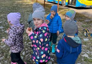 Dzieci jedzą upieczone na ognisku kiełbaski.