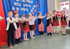 Dzieci stoją w półkolu i śpiewają piosenkę.