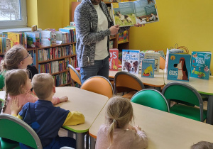 Bibloitekarz opowiada dzieciom o rodzajach książek zgromadzonych w bibliotece.