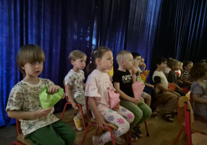 Dzieci siedzą na krzesełkach i jedzą popcorn