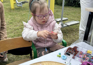 Dziewczynka robi bransoletkę z koralików.