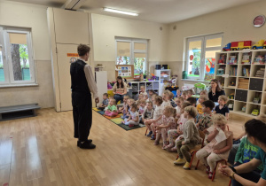 Dzieci siedzą w sali, przed nimi stoi muzyk